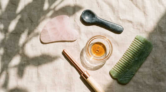 Vegan beauty tools including a rose quartz gua sha, stone facial tool, copper wand and jade scalp comb on oatmeal linen